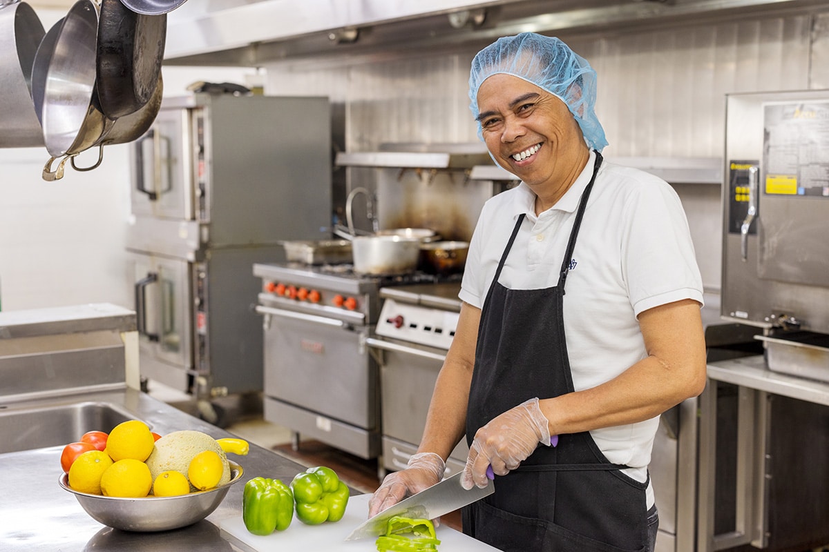 A Kitchen staff member cutting vegetables