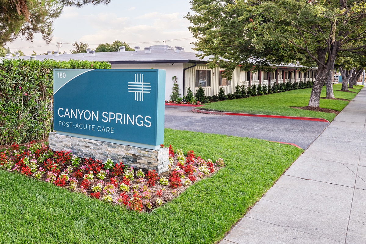 The front of the Canyon Springs facility with a monument sign and flowers and sidewalk